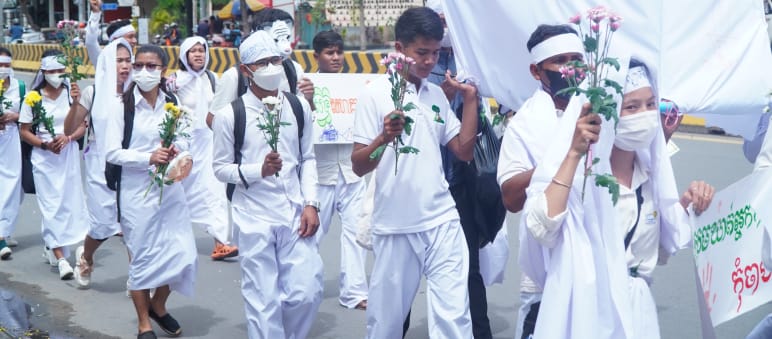 Weiß gekleidete junge Leute laufe mit Blumen in der Hand durch eine Straße in Phnom Penh
