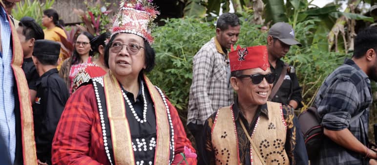 Frau mit roter Jacke und traditioneller Dayak-Kostümierung mit Mann in Weste aus Rinde