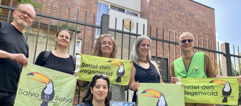 6 Personen stehen vor dem Gitter des Botschaftgebäudes, in den Händen haben sie Banner mit der Aufschrift Rettet den Regenwald und Salva la Selva mit dem Tukan-Symbol des Vereins
