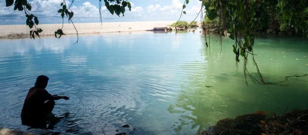 Dieses Paradies soll verschwinden - für die Zementproduktion Eine Frau sitzt im Wasser in einer von Felsen und Sandstrand gesäumten Bucht