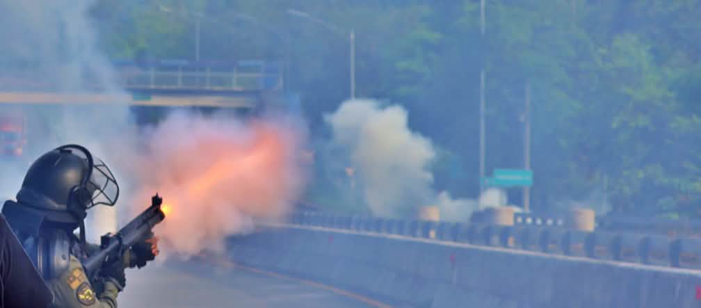 Ein Polizist in schwarzer Schutzkleidung verschiesst Tränengas mit einem Gewehr auf einer leeren Autobahn