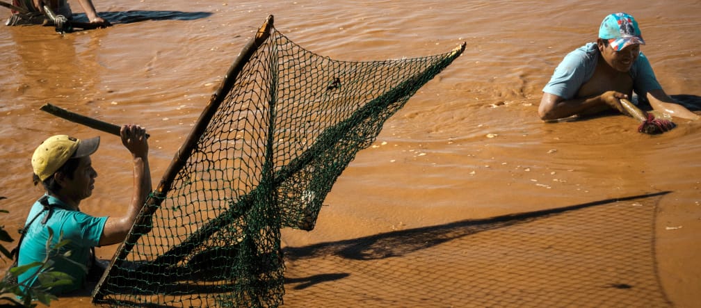 Drei Männer stehen zum Fischfang bis über die Hüften in den braunen Fluten eines Gewässers