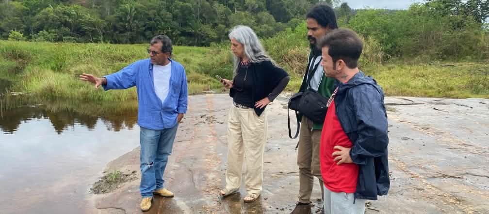 Vier Personen betrachten ein Gewässer vom Ufer aus