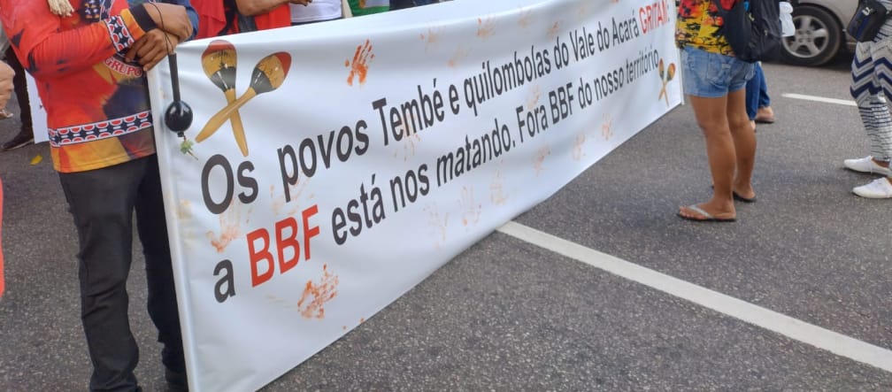 Eine Gruppe von Indigenen protestiert mit einem großen Banner auf einer Straße in einer Stadt: Aufschrift des Banners: Die Völker Tembé und Quilombola des Tales des Acará schreien. BBF tötet uns. BBF raus aus unserem Territorium