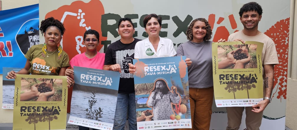 Sechs Personen halten Plakate mit verschiedenen Motiven und der Aufschrift "Resex Tauá-Mirim jetzt!" hoch.