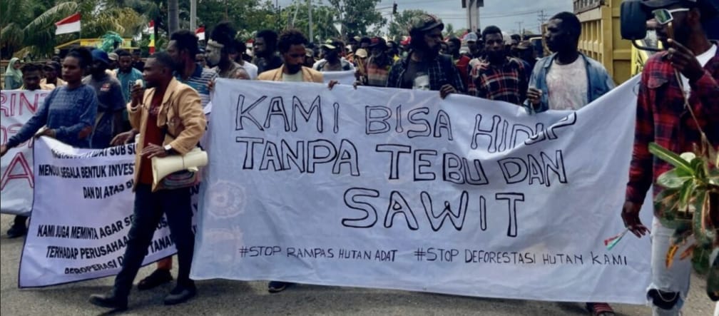Menschenmenge mit Banner: "Wir können ohne Zucker und Palmöl leben. Stop Raub des Indigenenwaldes. Stop die Abholzung unseres Waldes"