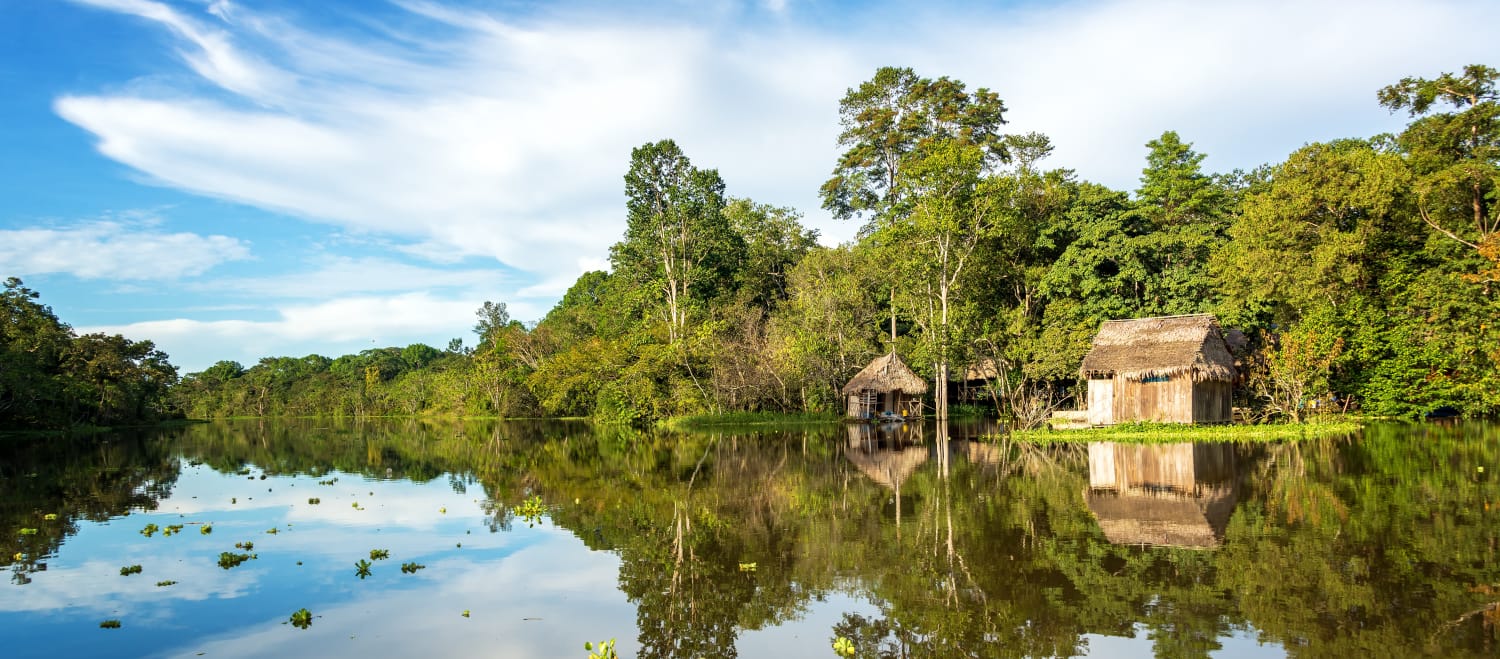 Der Amazonasregenwald und eine Holzhütte spiegeln sich im Wasser des Yanayacu-Flusses in Peru