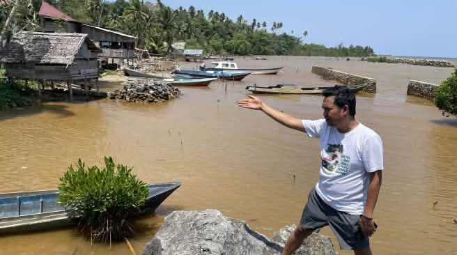 Ein Mann zeigt mit einer Hand auf die hinter ihm sichtbare Verschmuztung des Wasser an einer tropischen Küste