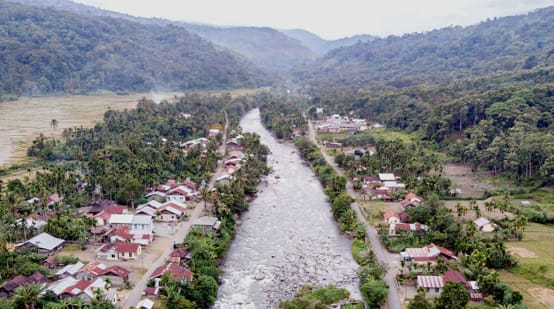 Fluss durch Dorf, im Hintergrund Berge
