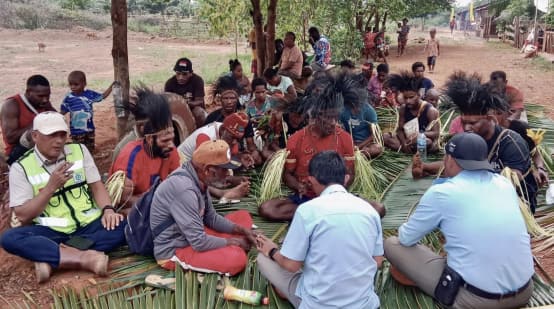 eine Gruppe Papua sitzt auf Palmblättern