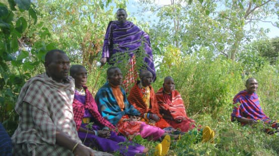 Gruppe Massai-Männer sitzt im Gras, gekleidet in bunte Decken