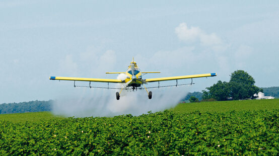 Ein Sprühflugzeug nebelt ein Sojafeld mit Pestiziden ein