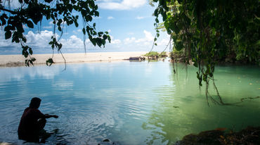 Eine Frau sitzt im Wasser in einer von Felsen und Sandstrand gesäumten Bucht