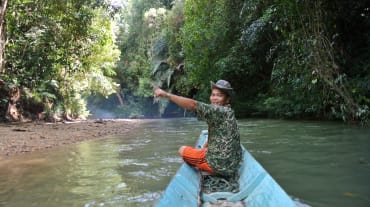 Ein Mann an der Spitze eines kleinen Bootes zeigt begeistert den Regenwald