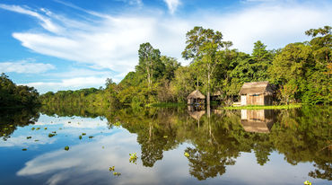 Der Amazonasregenwald und eine Holzhütte spiegeln sich im Wasser des Yanayacu-Flusses in Peru