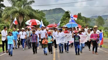 Demonstranten marschieren mit Bannern, Landesflaggen und Schirmen auf einer Landstrasse in Panama