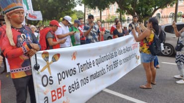 Eine Gruppe von Indigenen protestiert mit einem großen Banner auf einer Straße in einer Stadt: Aufschrift des Banners: Die Völker Tembé und Quilombola des Tales des Acará schreien. BBF tötet uns. BBF raus aus unserem Territorium