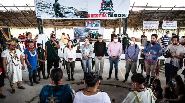 Zeremonie in einem Regenwalddorf: Eine Gruppe von Menschen bildet unter einem Banner einen Kreis