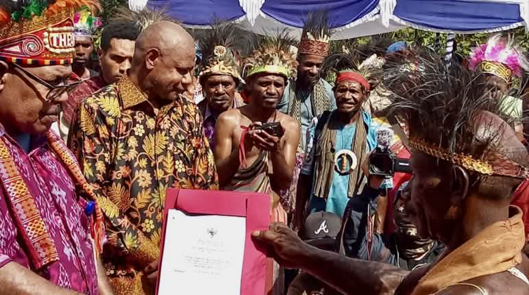 Die Urkunden zur Anerkennung als indigene Gemeinschaften und des indigenen Waldes werden in einer feierlichen Zeremonie überreicht. Eine Gruppe Papua in traditioneller Kleidung hält eine Urkunde