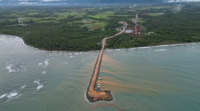 Ein brauner Schiffsanlegedamm führt von der Nickelmine im Regenwald ins Meer hinaus. Luftaufnahme