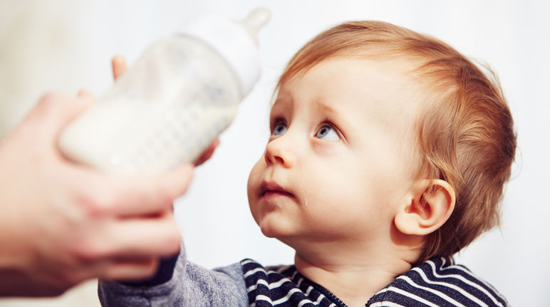 Kleinkind greift nach Babyflasche mit Milch