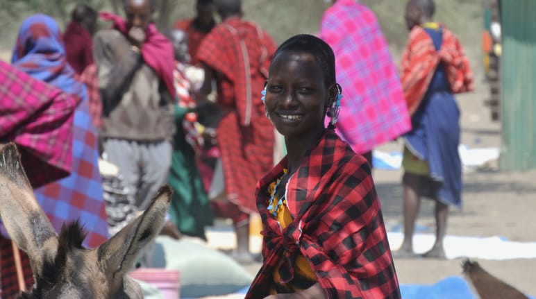Die Massai tragen ihre typische Kleidung und Schmuck auch im Alltag Frauen und Männer der Massai in bunten Tüchern auf einem Markt, eine Frau schaut in die Kamera