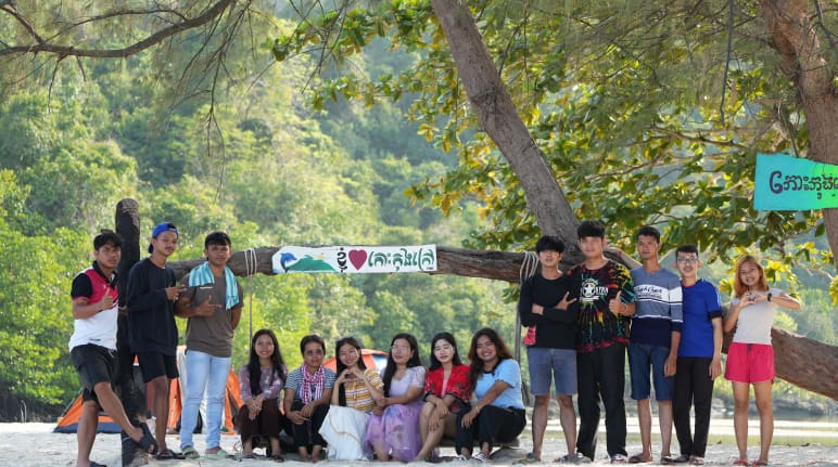 Mitglieder von Mother Nature Cambodia auf der Insel Koh Kong, die sie vor Zerstörung bewahren wollen Eine Gruppe junger Leute sitzt und steht vor einem Baum am Strand