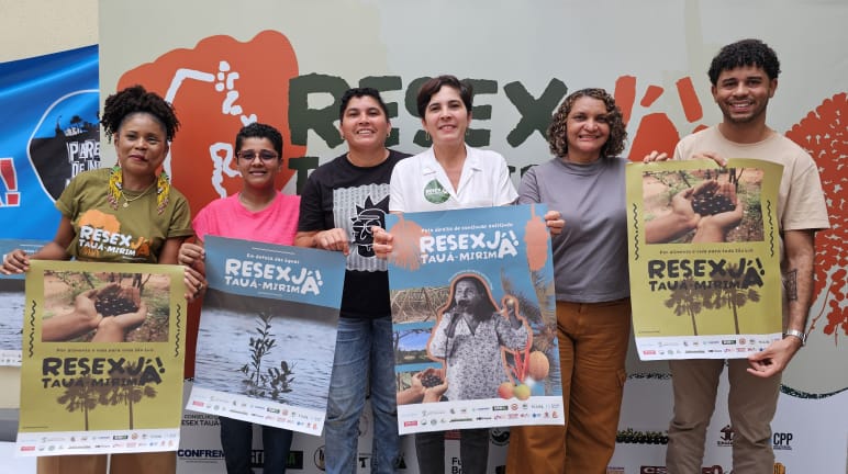 Sechs Personen halten Plakate mit verschiedenen Motiven und der Aufschrift "Resex Tauá-Mirim jetzt!" hoch.