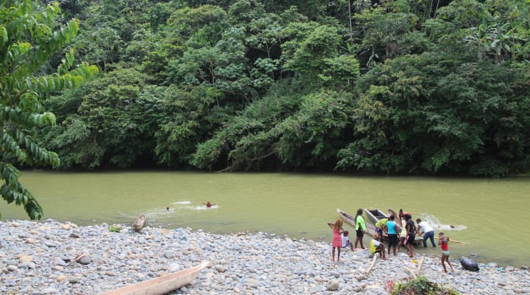 Personen und Kanus am Ufer eines Flusses im Regenwald sowie im Wasser schwimmende Kinder