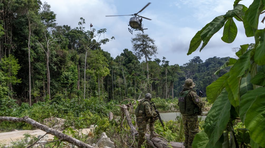 Zwei bewaffnete Männer in Tarnanzügen der Umweltbehörde IBAMA unter einem fliegenden Hubschrauber auf einer Rodung im Regenwald