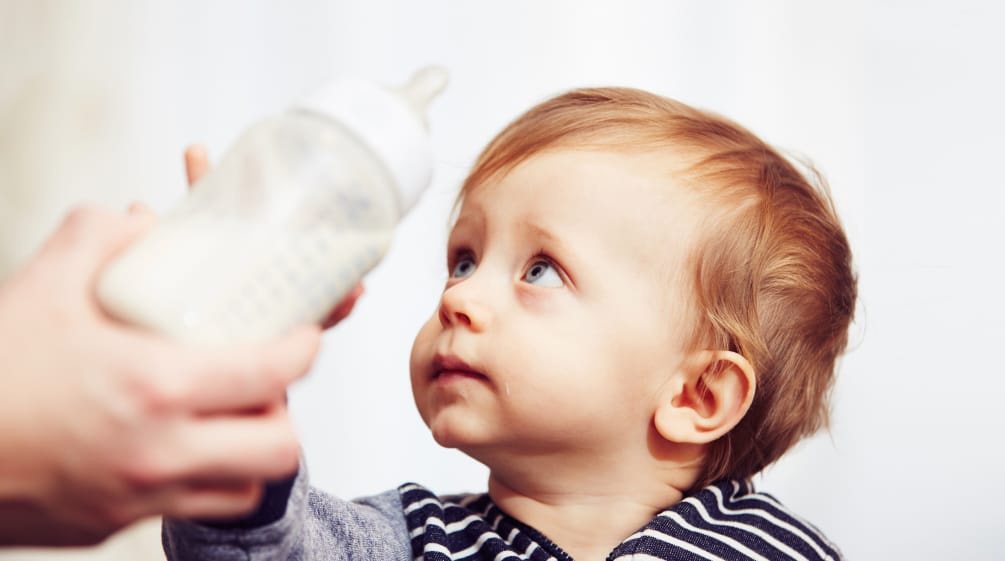 Verbraucherschützer gegen Palmöl Ein Baby wehrt mit sorgenvollem Blick eine ihm hingehaltene Trinkflasche ab