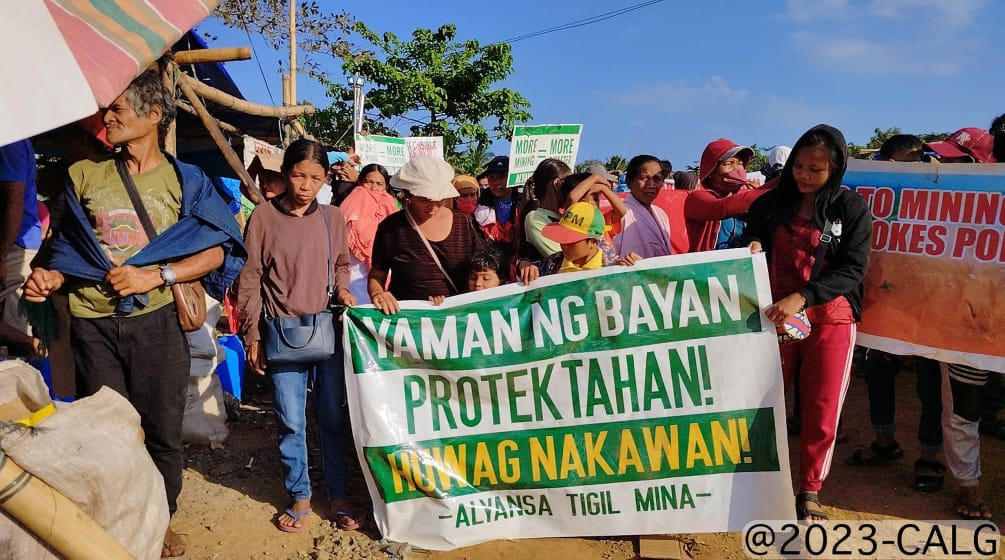Eine Gruppe von Menschen hält ein Plakat hoch, auf dem steht (übersetzt): Schützt den Reichtum des Volkes! Kein Raub! Allianz gegen Bergbau