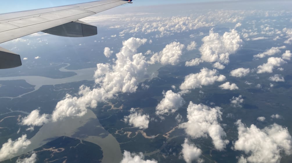 Blick vom Flugzeugfenster auf Wolken, Flüsse und Regenwald, oben im Bild der Flugzeugflügel