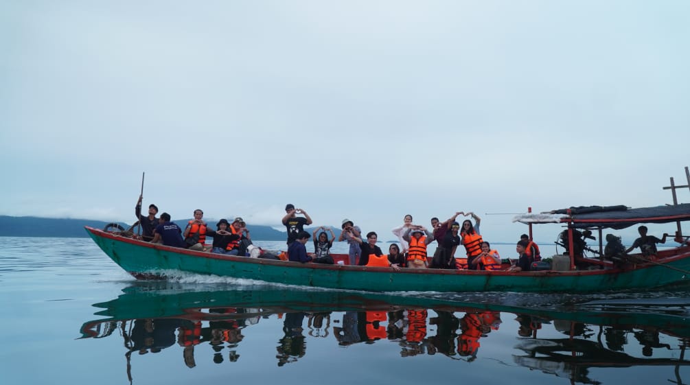 Viele Jugendliche sitzen und stehen auf einem langen schmalen Boot, das übers Meer fährtng Krao