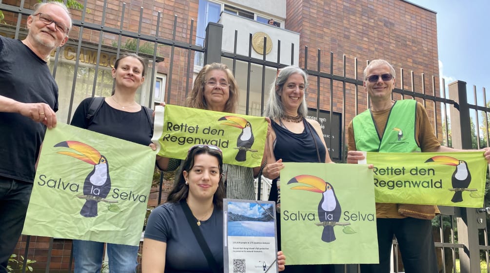 6 Personen stehen vor dem Gitter des Botschaftgebäudes, in den Händen haben sie Banner mit der Aufschrift Rettet den Regenwald und Salva la Selva mit dem Tukan-Symbol des Vereins