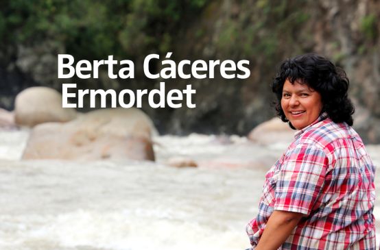 Die Umweltaktivistin Berta Cáceres sitzt auf einem Stein am Fluss und blickt über ihre Schulter in die Kamera