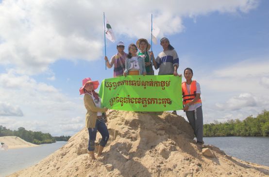 Umweltschützer stehen auf einem aufgeschütteten Sandhügel und halten ein Protestbanner hoch: Kampagne gegen Sandabbau in der ganzen Koh Kong-Provinz