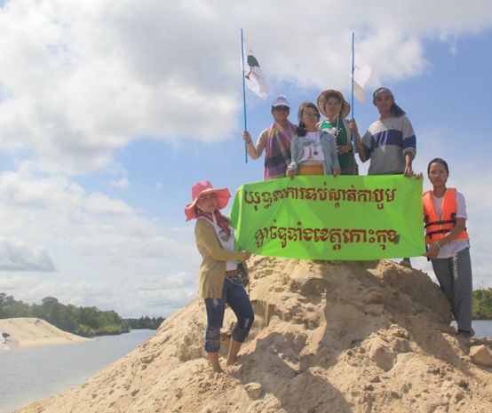 Umweltschützer stehen auf einem aufgeschütteten Sandhügel und halten ein Protestbanner hoch: Kampagne gegen Sandabbau in der ganzen Koh Kong-Provinz
