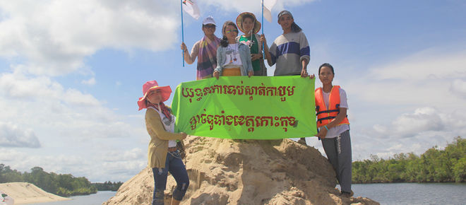 Umweltschützer stehen auf einem aufgeschütteten Sandhügel und halten ein Protestbanner hoch: Kampagne gegen Sandabbau in der ganzen Koh Kong-Provinz