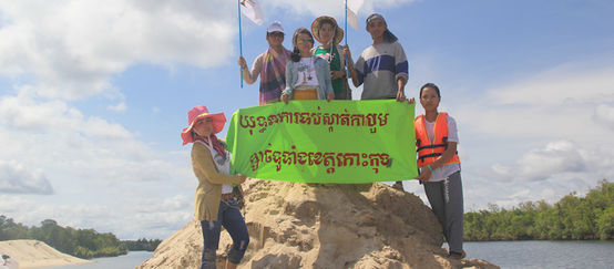 Umweltschützer stehen auf einem aufgeschütteten Sandhügel und halten ein Protestbanner hoch: Kampagne gegen Sandabbau in der ganzen Koh Kong-Provinz