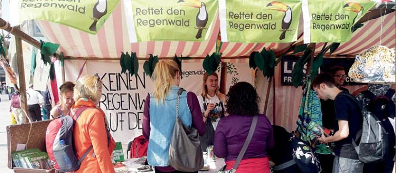 Besucher stehen vor dem bunt-geschmückten Informationsstand von Rettet den Regenwald