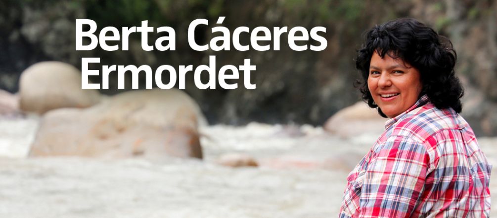 Die Umweltaktivistin Berta Cáceres sitzt auf einem Stein am Fluss und blickt über ihre Schulter in die Kamera