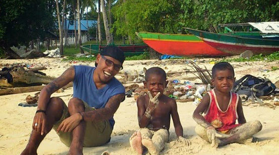 Jopi Peranginangin sitzt mit zwei kleinen Jungen am Strand und lacht in die Kamera