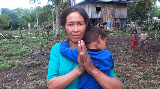 Eine Frau mit Kind auf dem Arm steht vor ihrer provisorisch aufgebauten Hütte. Von ihrem eigenen Land wurde sie vertrieben