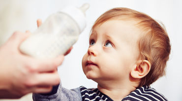 Kleinkind greift nach Babyflasche mit Milch
