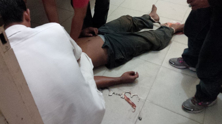 Die Leiche eines schwerverletzten Manns liegt auf dem Boden. Sein Kopf ist verdeckt. An seinen Händen sind Handschellen.