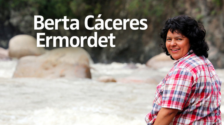 Die Umweltaktivistin Berta Cáceres sitzt auf einem Stein am Fluss und blickt über ihre Schulter in die Kamera