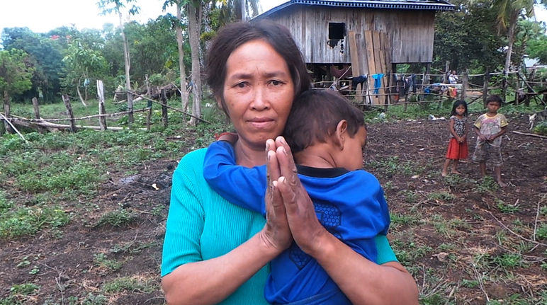 Eine Frau mit Kind auf dem Arm steht vor ihrer provisorisch aufgebauten Hütte. Von ihrem eigenen Land wurde sie vertrieben