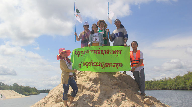 „Stoppt den Sandabbau in der Provinz Koh Kong“, fordern die Umweltschützer von Mother Nature Umweltschützer stehen auf einem aufgeschütteten Sandhügel und halten ein Protestbanner hoch: Kampagne gegen Sandabbau in der ganzen Koh Kong-Provinz