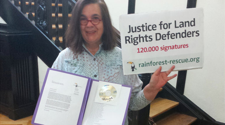Rettet den Regenwald übergibt 120.000 Unterschriften zur Unterstützung der Landrechtskämpfer in SIerra Leone. Eine Aktivistin von Rettet den Regenwald hält in der Botschaft von Sierra Leone Petition und Übergabeplakat in die Höhe.